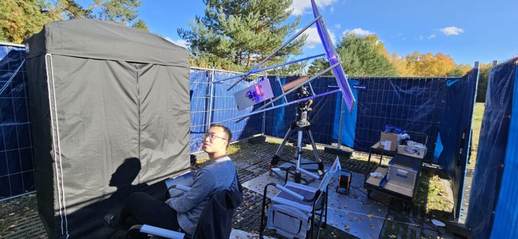 Cheng Li is shown with the outdoor experimental setup. The sunlight concentration module, including the Fresnel lens and the solar concentrator, is mounted on a solar-tracking motor to ensure stable power delivery. The entanglement generation and detection setup, including the nonlinear crystal and the single-photon detectors, are shielded in an optical enclosure placed inside a blackout tent. Credit: Jasvinder Brar, Max Planck Institute for the Science of Light