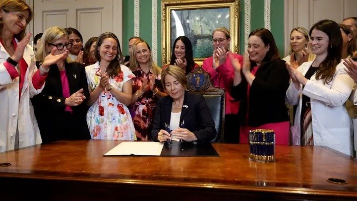 Women smile and applaud as Massachusetts Gov. Maura Healey signs legislation allowing babies to be aborted up to birth. (@MassGovernor/X)