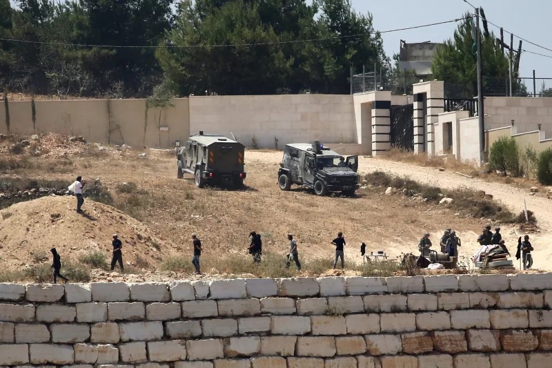 Israeli soldiers stand guard next to settlers in front of Palestinian homes that they have blockaded in the village of Qusra, south of Nablus, in the occupied West Bank, Wednesday, Aug. 12, 2026. Nidal Eshtayeh/AP